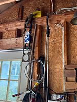 Photo capturing various tools including long metal rods, flexible shaft tool, and red grease gun hanging on a wooden wall near a door.