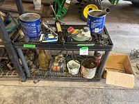 Shelf with cans, hoses, chains, metal hardware, and various small parts and tools. Visible rust and dust.