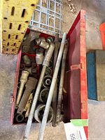Overview of red toolbox filled with large heavy duty sockets and long socket extensions or breaker bars made of steel, showing wear and dirt.