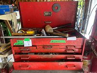 Front view of the red metal toolbox open, showing the upper compartment with some loose tools inside and the five drawers below.