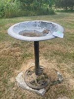 Front angle view of the metal birdbath showing scalloped edge basin and metal base on stone.