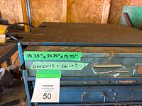 Front of the blue metal parts cabinet showing four drawers with handles and labels, with visible rust and paint wear.