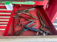 Drawer with various used hand tools including locking pliers, needle nose pliers, wire cutters with rubber grips, and pincers showing signs of rust and dirt.