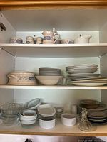 Shelf display showing mixed stoneware, glass, ceramic dishes and serveware in beige and blue pattern, clear glass bowls, and white ramekins