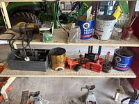 Shelf holding assorted tools, metal cans used as hardware containers, cordless drill, wrenches, jack stands, and other workshop items.