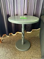 Full view of the painted wood side table showing round top, spindle designed center column, and circular base set against curtain backdrop.