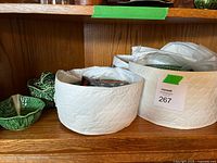 Set of cabbage leaf ceramic dishware pieces in white quilted holders on wooden shelf