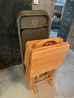Wooden folding tray tables and metal folding chairs stacked together, showing the materials and condition