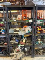 Full view of black metal shelving unit filled with assorted tools and equipment in a workshop setting.