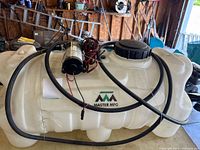 Overall view of white sprayer tank with Master MFG logo, pump mounted on top and coiled hose and wiring
