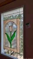 Stained glass window panel hanging in window with white tulip design and green leaves. Cream border. Hanging chain visible.