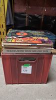 Stack of vinyl records visible inside a red plastic crate with some titles readable such as Neil Diamond's Greatest Hits.