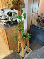 Full view of the large wicker giraffe planter standing indoors, showing the potted plant vine wrapped around the neck.