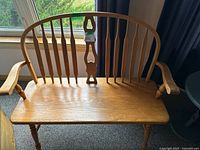 Full view of the Windsor style wooden bench showing its curved spindle backrest, smooth seat, and armrests.