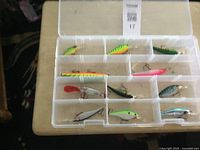 View of the fishing lures arranged in a plastic tackle box with clear compartments, showing various colors and styles of lures.