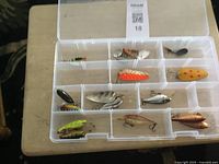 Clear plastic tackle box with 12 fishing lures of different shapes and colors arranged in compartments.