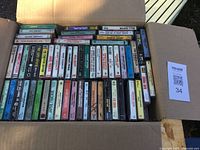 Box filled with cassette tapes arranged in rows, showing assorted titles and artists.