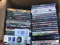 Photo showing top and side views of two stacks of DVD movies in a cardboard box with visible titles of various movies.