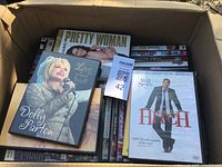 Cardboard box filled with 30 DVD movies including Pretty Woman, Hitch, and Dolly Parton Live and Well concert DVD.