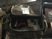 Top view of the opened camouflage fishing tackle bag showing various fishing accessories inside including a red and black tool and packaged hooks and line.