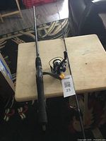 Photo of Quantum Iron Fire fishing rod and spinning reel on a wooden table, showing the entire assembled fishing rod with foam grip handle and metal line guides, reel attached.