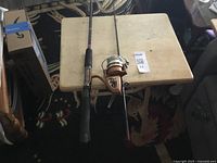 Full assembled fishing rod with spinning reel lying flat on a small square table, with rod handle and reel clearly visible.