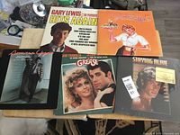 Five LP vinyl albums laid out on a patterned rug including titles Gary Lewis & The Playboys - Hits Again, American Gigolo, Grease, Staying Alive, and one with a waitress illustration on cover.