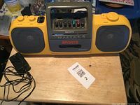 Front view of yellow Sony Sports Sports Boom Box placed on a wooden surface showing the cassette player, speakers, and control buttons