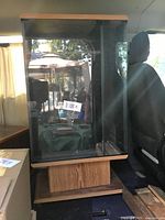 Stereo stand photo showing the front and side glass panels with wood base on wheels inside a vehicle.