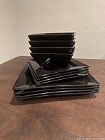 Stack of square plates and bowls showing glossy black ceramic material and square shape.