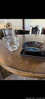 Photo showing set of three items on a wood table: clear glass bowl, black ceramic bowl, black square tray