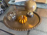 Photo showing all items on a glass table including brass tray, globe, pumpkin figure, and glass votive holder with candle wax.