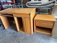 Photo of desk and matching nightstand in light oak veneer finish, showing the overall structure and color of both items in a warehouse setting.