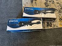 Two boxed Detroit Axle complete strut assemblies side by side on floor showing product image and brand name on boxes.