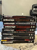 Stack of Entourage DVD box sets for all 7 seasons, including Season 3 split into two parts. Spine labels visible with season titles.