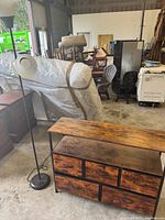 Side view of the black metal floor lamp with white plastic shade and 5-drawer dresser with wooden front and metal frame