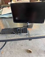 LG monitor and Dell wired USB keyboard placed on a glass outdoor table with cable loosely coiled.