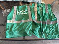 Green mesh safety vests with reflective stripes laid out flat, showing front and back, branded LGCNS (M Solution)
