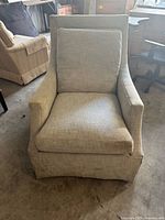 Front view of light grey upholstered armchair with removable cushions, showing straight back and skirted base.