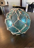 Close-up of a medium-sized turquoise glass float with natural rope netting, spherical shape.