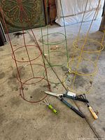 Three circular plant supports in red, green, and yellow with two garden hand tools on the ground in front of them