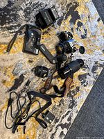 Photo shows entire lot contents including two vintage film cameras, lenses (80-200mm zoom and 50mm prime), Pentax flash, camera strap, cables, and battery holder arranged on a carpet.