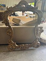 Front view of ornate framed mirror showing detailed scroll and floral carved frame with crest top.
