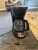 Full view of black Mr. Coffee drip coffee maker with glass carafe and digital control buttons on the base, power cord visible.