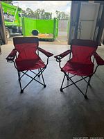Pair of red Ozark Trail folding armchairs with cup holders shown indoors on floor, visible steel frame and fabric seat and backrest.