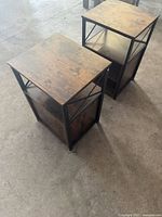 Pair of brown wood topped end tables with black metal X-shaped frames, shown from above and angled to display wood finish and metal structure.