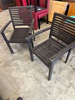 Two dark brown/black wooden armchairs with horizontal slatted design on seats and backs, photographed on concrete floor with visible scratches and minor paint wear.
