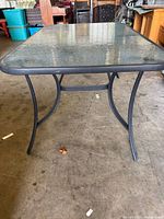 Full view showing rectangular textured glass tabletop with metal frame and curved legs on concrete floor.