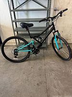 Full side view of Rock Rider mountain bike showing black and teal frame, front suspension fork, saddle, pedals, and tires.