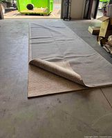 Full view of large rectangular area rug laid flat with one corner slightly folded to show texture and thickness.